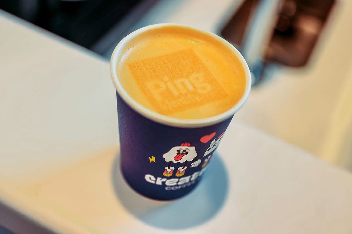 A photo of a cup of coffee with the Ping Identity logo stamped in the foam on top.