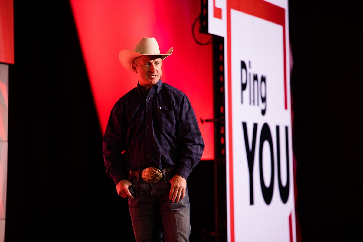 A photo of Cord McCoy, PBR Champion and Finalist on The Amazing Race, wearing a cowboy hat while addressing the crowd from the stage.