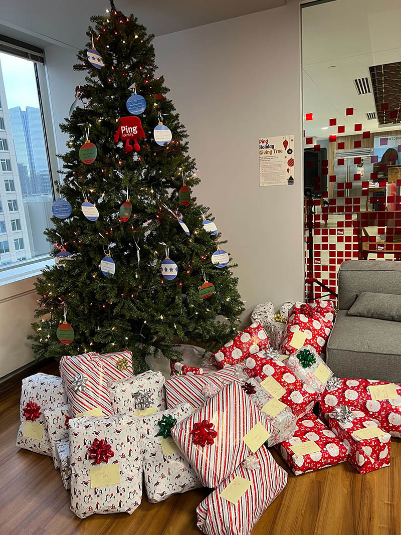 A photo of a Ping Identity-branded Christmas tree with many wrapped gifts at its feet at the Denver Ping office.