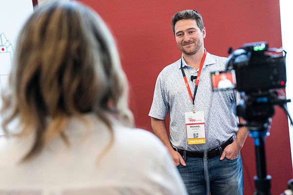 conference attendee standing behind camera being interviewed