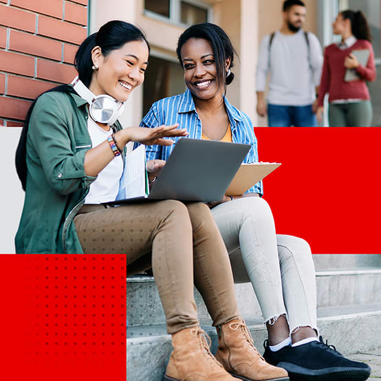 Two women with laptops sitting on college steps talking and laughing