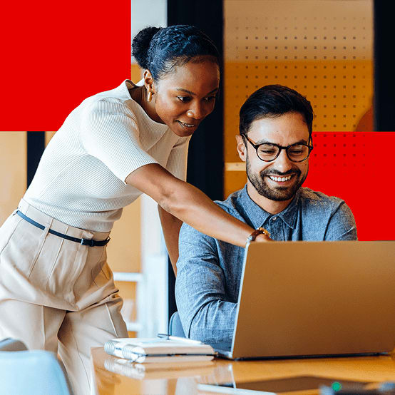 Woman looking over mans shoulder while pointing at laptop screen