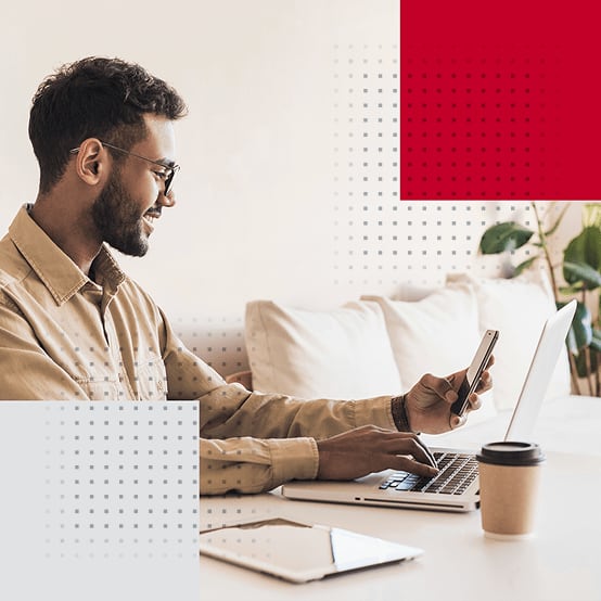 Man smiling while looking down at his phone and working on laptop