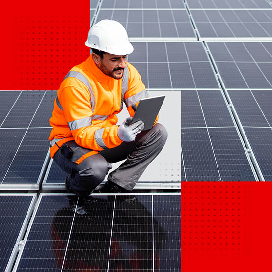 Worker in safety gear inspecting solar panels with a tablet