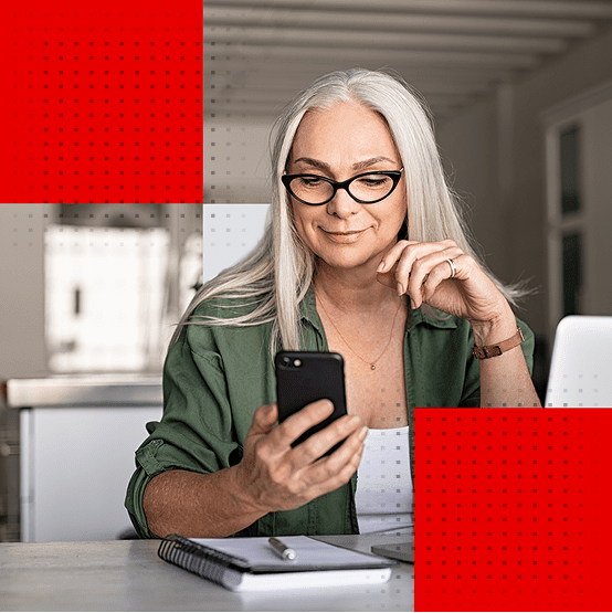 Woman smiling while looking at her phone beside a laptop