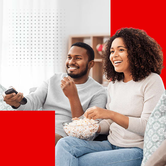 A smiling couple sitting on a couch eating popcorn and watching TV