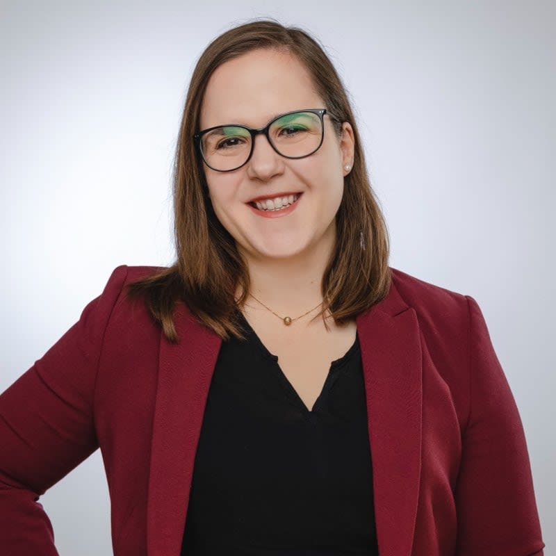 Smiling woman with glasses wearing a maroon blazer