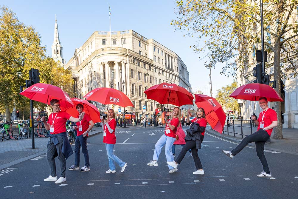 Group holding red umbrellas crossing sunlit urban street
