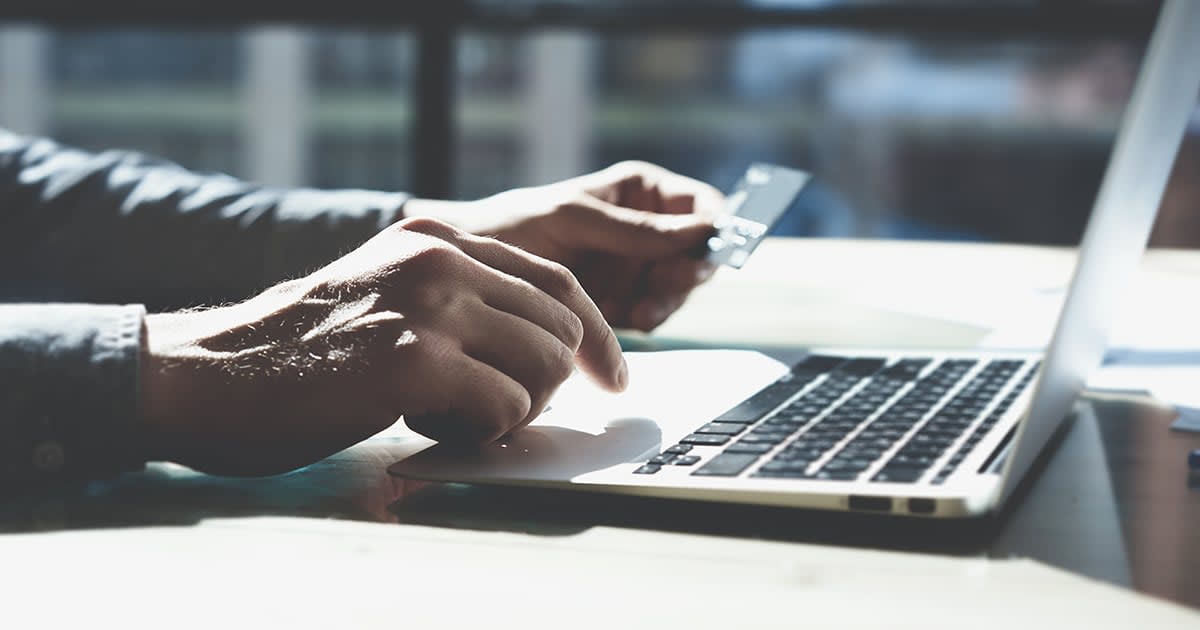 Image of hands (man) at a laptop holding a credit card 