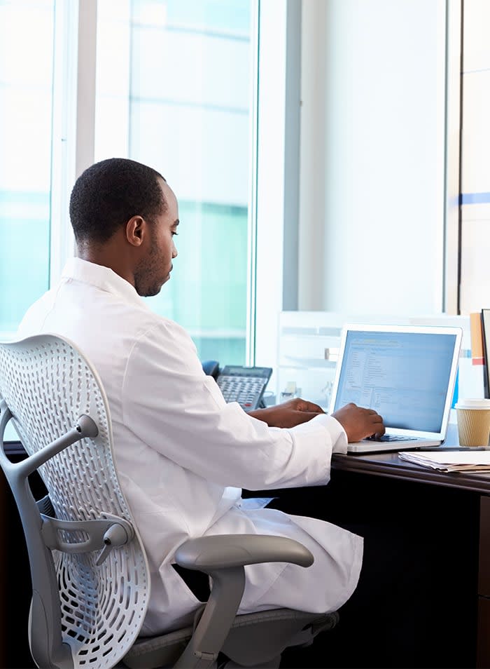 Man in a lab coat sitting at a desk while looking at a laptop computer