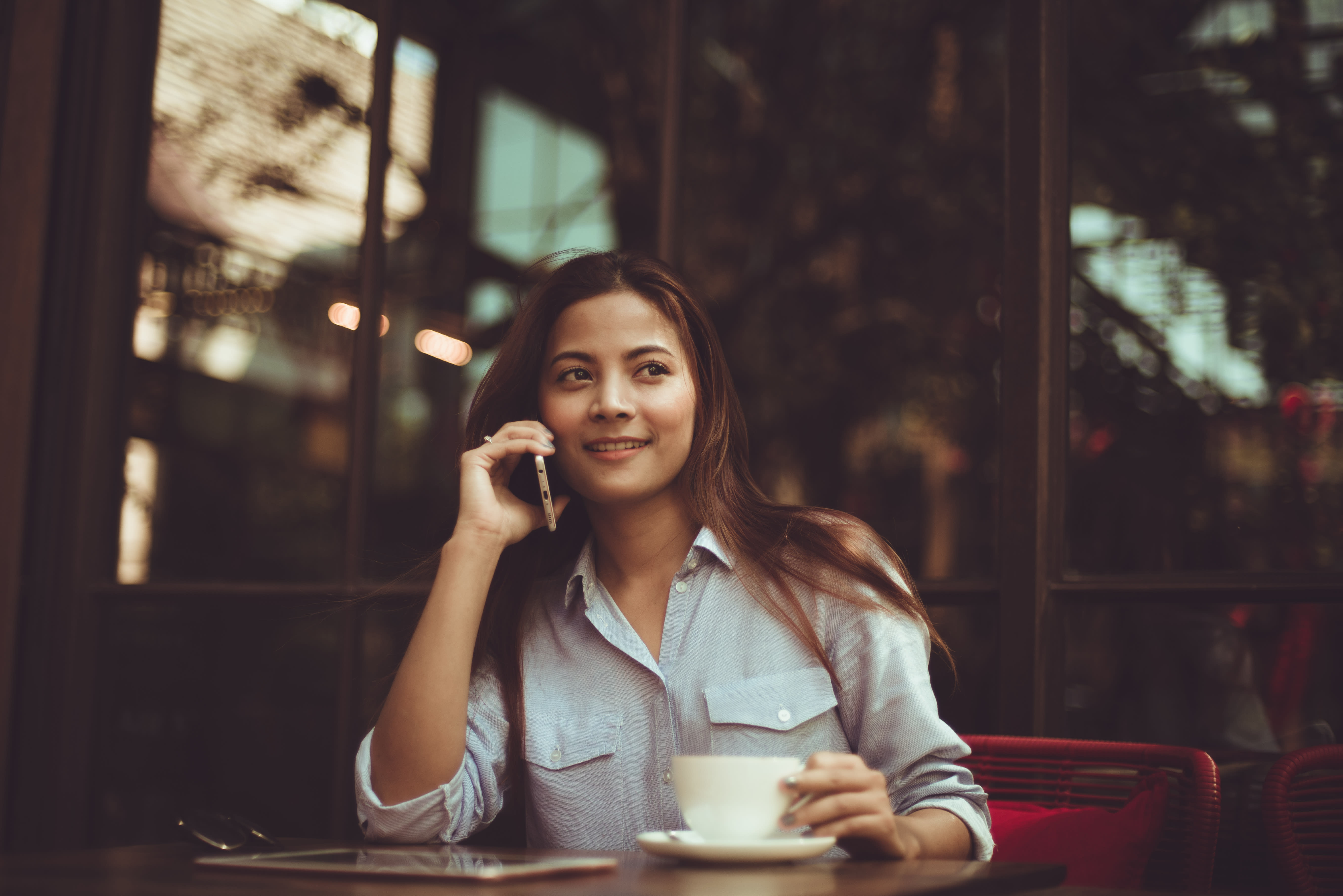 Image of a woman sitting down having a cup of coffee while talking on the phone.
